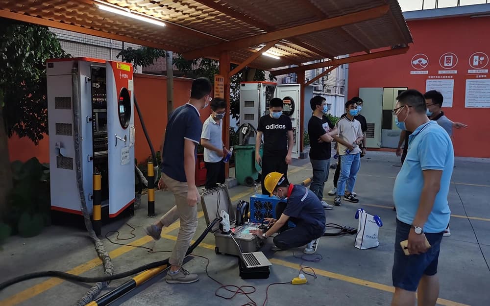 Technicians operating charging test equipment beside DC chargers at a sheltered charging station