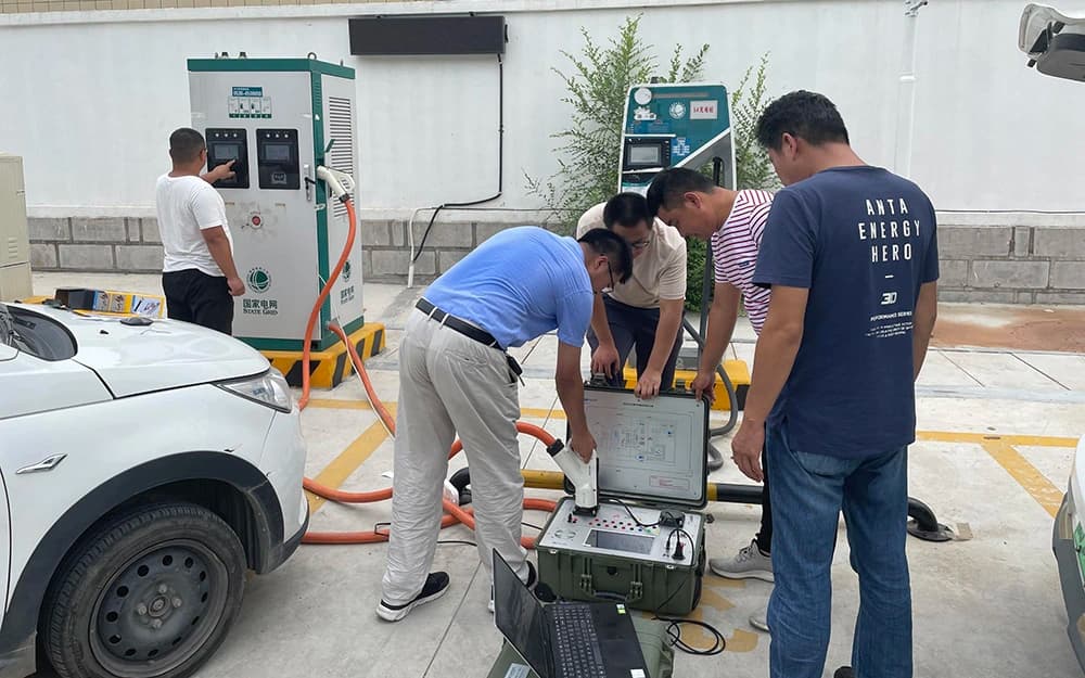 Technicians examining charging test equipment beside an electric vehicle and charging station